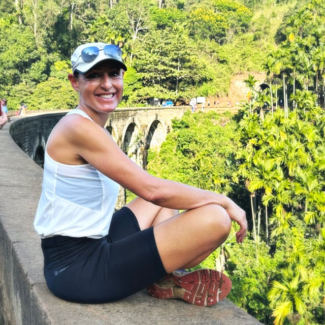 Andrea Elber - sitzend auf einer Brücke und in die Kamera lächelnd